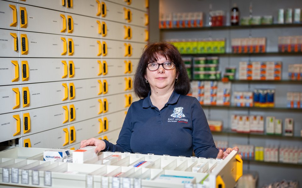 Eine Mitarbeiterin der Knut Apotheke im dunkelblauen Poloshirt an einer geöffneten Schublade mit Arzneimittelpackungen.