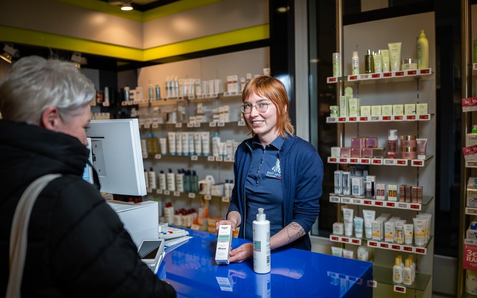 Eine Mitarbeiterin der Knut Apotheke am Handverkaufstisch im Gespräch mit einer Kundin, auf dem Tisch liegt das Kartenterminal.
